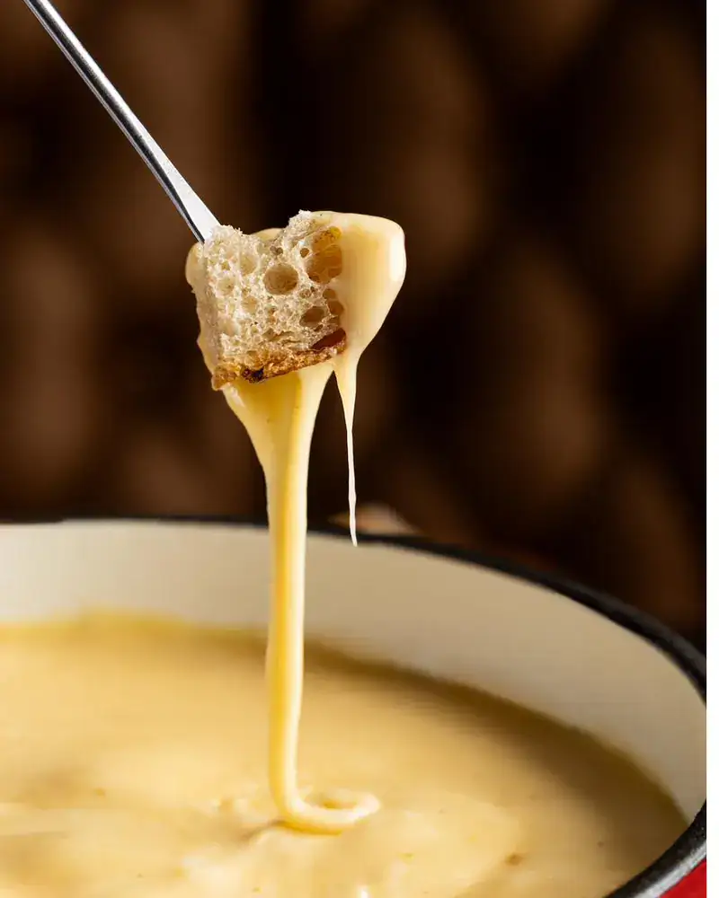 Pão mergulhado na fondue de queijo da Hannover, com o fio de queijo derretido esticando