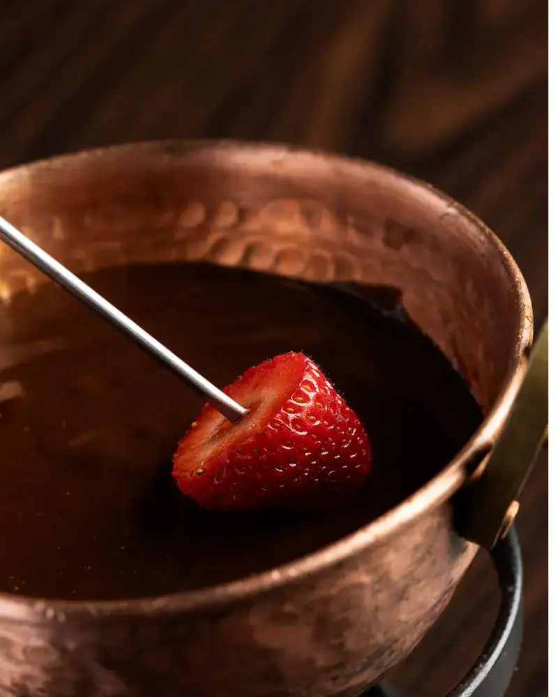 Morango mergulhado na fondue de chocolate servida na panela de cobre da Hannover