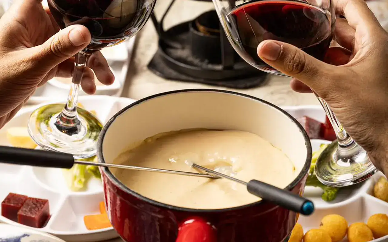Casal brindando com taças de vinho sobre a panela de fondue de queijo na Hannover